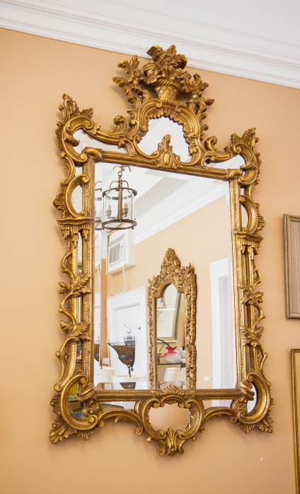 $1,495. Elaborately carved gilt wood beveled mirror decorated with scrolling and leaf details, surmounted by a floral bouquet. Mirrors set between the gilt wood elements.